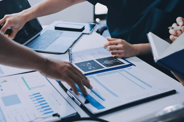 Two doctors and a female nurse meet at a table in the hospital, collaborating on medical tasks using laptops and computers