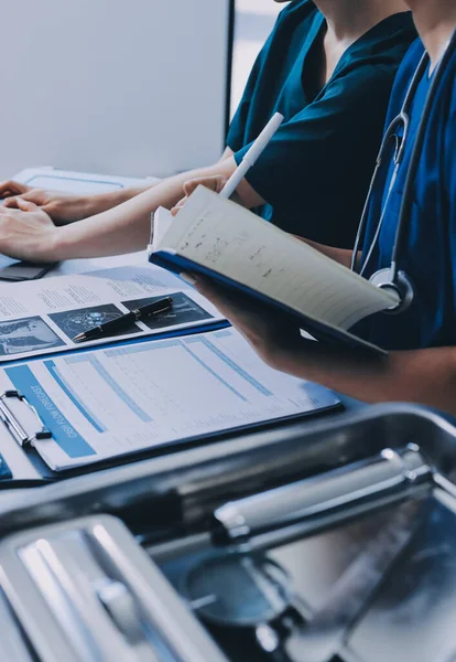 Two doctors and a female nurse meet at a table in the hospital, collaborating on medical tasks using laptops and computers