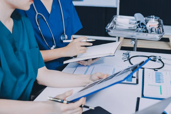 Two doctors and a female nurse meet at a table in the hospital, collaborating on medical tasks using laptops and computers