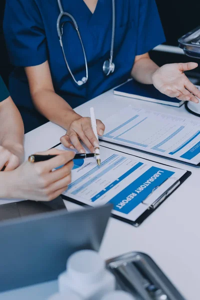 Medical team meeting analyzing blood test results in hospital laboratory. Doctors and scientists in lab coats are having a discussion about blood test result, holding test tubes and taking notes.