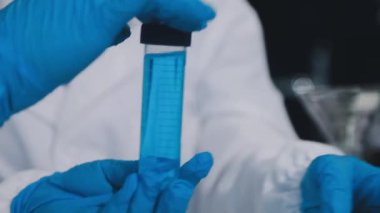 Yakın plan. Elinde test tüpü tutan mavi eldivenli bir el.