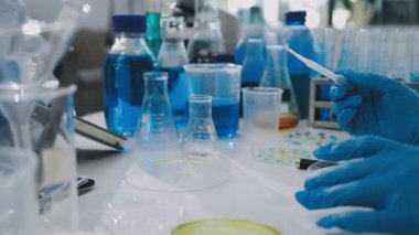 Laboratuvarda koruyucu eldivenli bir bilim adamı cep şişesi tutuyor..