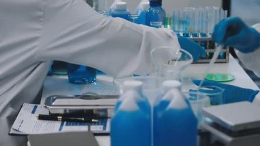 Mavi takım elbiseli bilim adamları laboratuarda test tüpleri tutuyor.