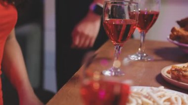 Masanın üzerinde bir kadeh kırmızı şarap ve bir şişe şampanya, bir bardak şarap ve bulanık bir arka planda bir dilim pizza.