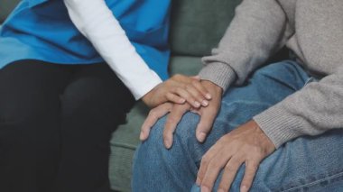 Genç bir kadın ve bir adam kanepede oturuyor ve bir odada el ele tutuşuyorlar.