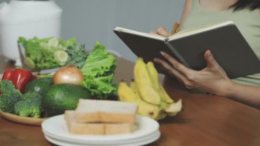 Oturma odasında sağlıklı yemek yerken kitap okuyan bir kadın.