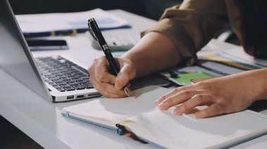 Bilgisayarda çalışan ve ofiste notlar alan genç bir kadın..