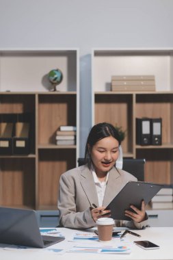 Asyalı iş kadını şirketin başarısı hakkında mutlu bir şekilde çalışıyor, finansal raporu analiz etmeyi planlıyor, iş planı yatırımı, finans analizi kavramı.