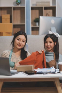 Genç Asyalı kadınlar müşterilerden gelen yeni siparişten sonra mutlu olurlar. Asyalı bir kadının online mağazasının satışındaki başarısının sürpriz ve şok edici yüzü. Çevrimiçi satış. Çevrimiçi Alışveriş