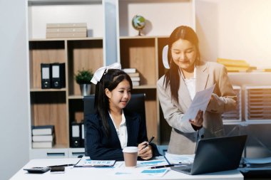 Two young Asian business woman talk, consult, discuss working with new startup project idea presentation analyze plan marketing and investment in the office.