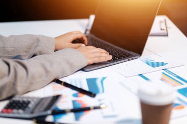 Hesap makinesi ve yazı kullanan bir iş kadını, hesap makinesiyle not alır. Ofiste çalışan bir kadın. Masasında dizüstü bilgisayar ve belgeler var.