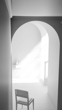 Kemerli bir geçitten geçen yumuşak güneş ışığıyla parlak bir koridora yerleştirilmiş, minimalist ve rahatlatıcı mimari bir iç mekan oluşturan, 3 boyutlu sakin bir sandalye..