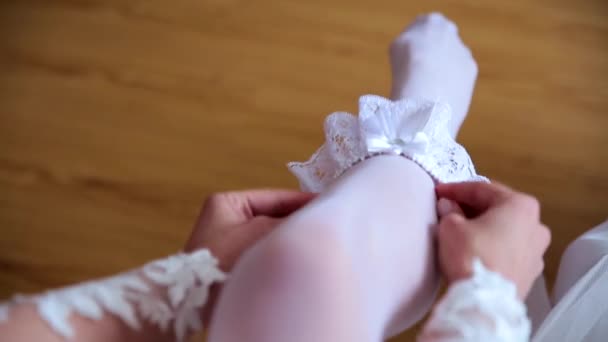 Nő a harisnyakötő viselése a lábát. A menyasszony tart a kezében veszíteni-up harisnyakötő szállodai szobában. reggel készítmény esküvői koncepció. — Stock videók