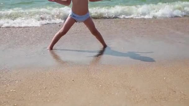 Enfant jouant sur une plage. Un gamin qui saute dans les vagues. Vacances en mer pour les familles avec enfants. Petit garçon courant sur la plage tropicale d'une île exotique pendant les vacances d'été . — Video