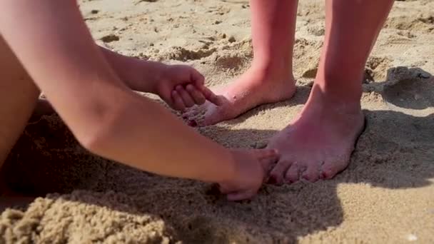 Il ragazzo si addormenta nella sabbia sul lungomare, con le dita sulla gamba della madre. Vacanza al mare per famiglie con bambini . — Video Stock
