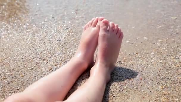 Un garçon est assis au bord de la mer et attrape les vagues. Les vagues lavent les pieds des garçons. Vacances en mer pour la famille avec enfants . — Video