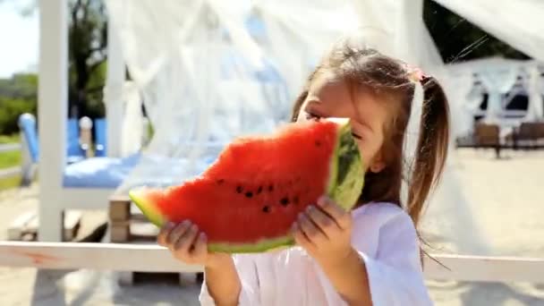 快乐快乐的小女孩 穿着白衣 在海滩上玩 吃西瓜 — 图库视频影像