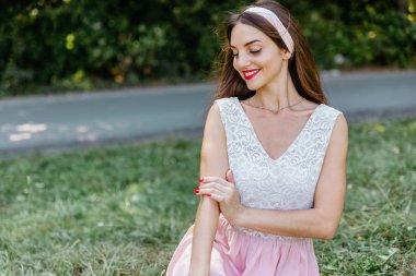 Bluz ve saç bandı içinde zarif, büyüleyici, seksi, güzel esmer kız yaz parkında yeşil çim üzerinde oturan pozlar