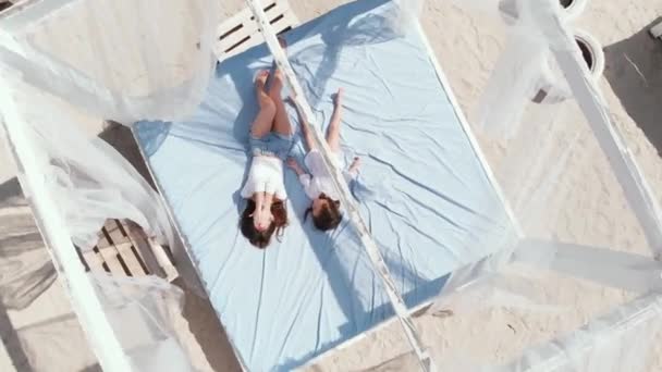 Chica exquisita con su hijita relajándose y jugando en bungalows en la playa . — Vídeo de stock