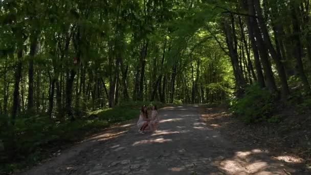 Elegante chica con su hija pequeña caminando y divirtiéndose en el bosque entre los árboles . — Vídeo de stock