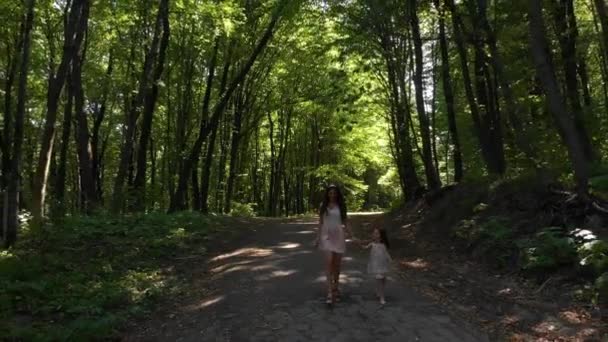 Elegantes Mädchen mit ihrer kleinen Tochter, die im Wald zwischen den Bäumen spazieren geht und Spaß hat. — Stockvideo