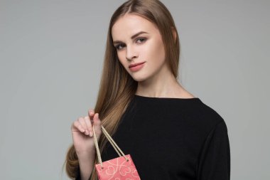 Genç model, uzun saçlı, siyah elbiseli sarışın kız elinde kırmızı kağıt hediye paketi tutuyor.