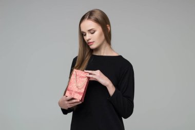 Genç model, uzun saçlı, siyah elbiseli sarışın kız elinde kırmızı kağıt hediye paketi tutuyor.