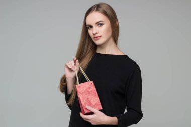 Genç model, uzun saçlı, siyah elbiseli sarışın kız elinde kırmızı kağıt hediye paketi tutuyor.