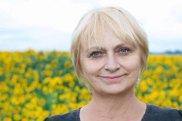 Headshot portrait of smiling aged retired blond white woman with direct sight of green blue eyes looking into camera