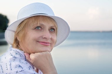 Mutlu gülümseyen yaşlı kadın nehir kıyısında dinleniyor.