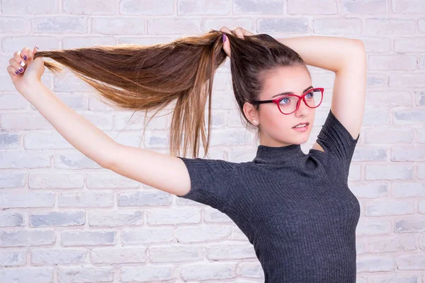 Chica joven en gafas rojas tira de su pelo largo Imagen de archivo