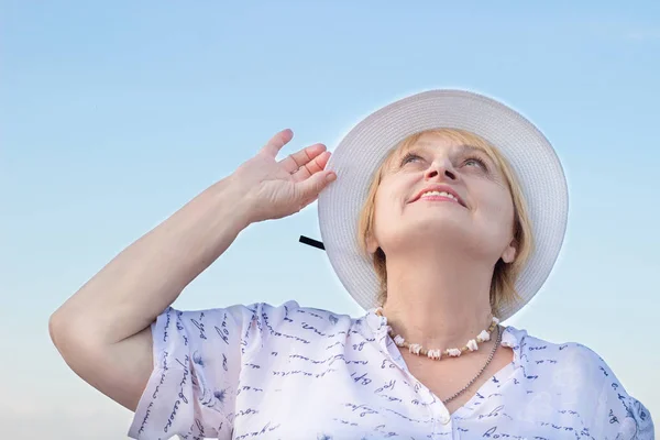 Smiling retired lady watches sky holding her white hat