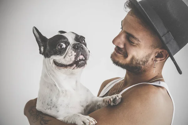 Tattooed boy with piercings with French Bulldog dog in his arms on white background