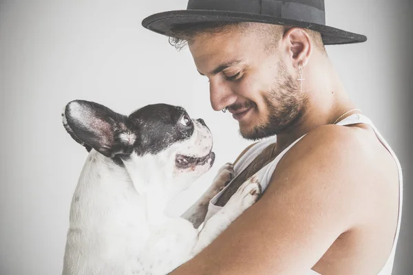 Tattooed boy with piercings with French Bulldog dog in his arms on white background