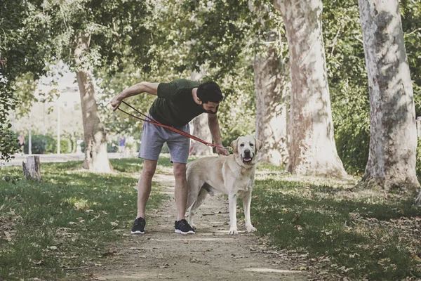 Young sportsman walking with his canadian labrador dog through an urban park on a sunny day
