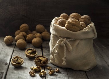 Ceviz ahşap bir masa üzerinde bir çantada. Masanın üzerine dağılmış birkaç fındık.