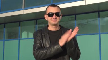Deri ceket ve güneş gözlüğü açık ve alkışlar veya alkışlayan duran genç adam