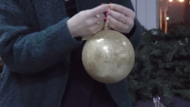 Uma mulher em uma camisola de lã verde quente brilhante segurando um brinquedo bolas douradas nas mãos — Vídeo de Stock