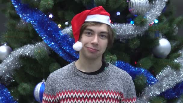 Lächelnder gutaussehender Mann mit Weihnachtsmütze, der Ja sagt, indem er auf dem Hintergrund des Weihnachtsbaums den Kopf schüttelt. — Stockvideo