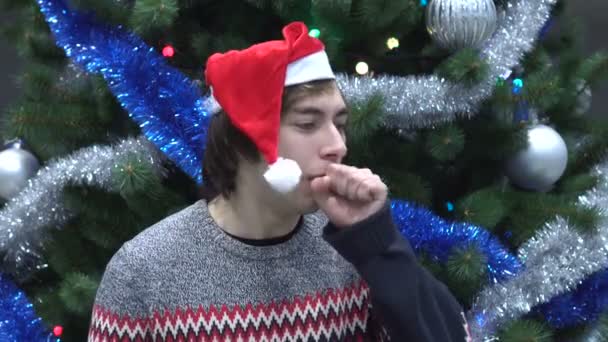Bonito jovem vestindo chapéu de Santa e tosse no fundo da árvore de Natal . — Vídeo de Stock