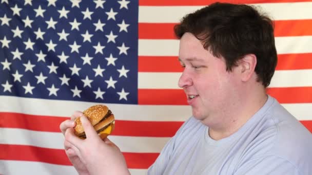 Man met een hamburger met een Amerikaanse vlag achtergrond. Grote kerel wil Fast Food — Stockvideo