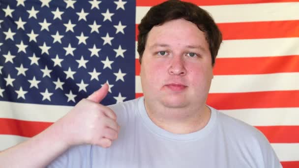 Big man showing thumbs up on the background of an USA flag. Young man showing like sign with hand — Stock Video