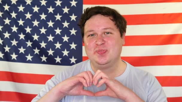 Gelukkig dikke man in liefde maken hart met vingers en glimlachend op de achtergrond van een USA vlag — Stockvideo