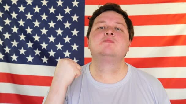 Joven hombre grande amenazadoramente mostrando su puño. Retrato en el fondo de una bandera de EE.UU. — Vídeo de stock