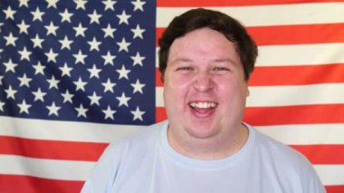 Genç adam bir Amerikan bayrağının arka planında gülüşünü tutuyor.