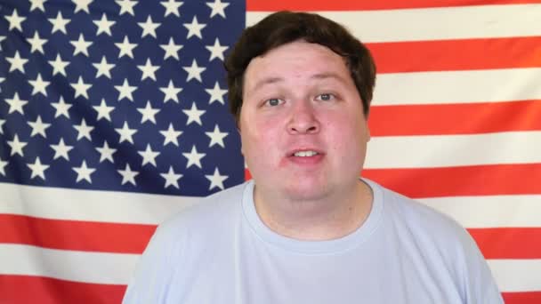 Young man talking about something on the background of an USA flag. — Stock Video