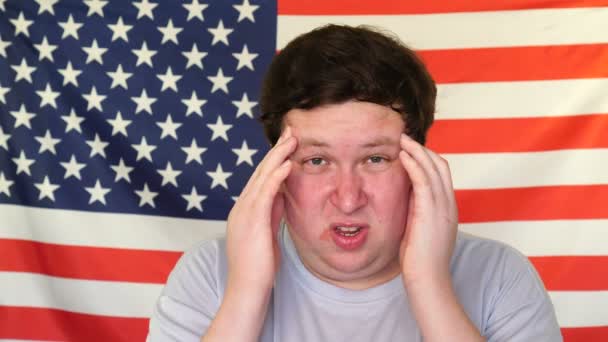 Jovem com dor de cabeça no fundo de uma bandeira dos EUA — Vídeo de Stock