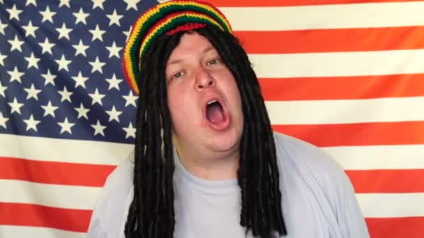 Happy rasztafári ember táncol és énekel reggae a háttérben egy amerikai zászló — Stock videók