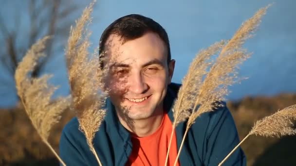 Портрет красивого улыбающегося мужчины с сухой травой, камыш на открытом воздухе — стоковое видео