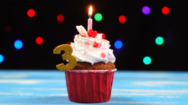 Delicious birthday cupcake with burning candle and number 3 on multicolored blurred lights background — Stock Video